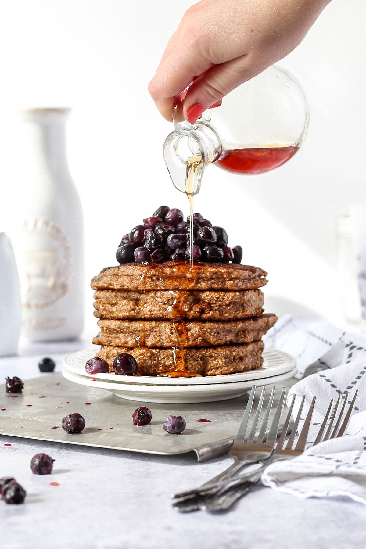 a stack of oat flour pancakes with blueberries on top and syrup drizzling down the side