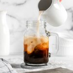 pouring almond milk into a glass of iced coffee