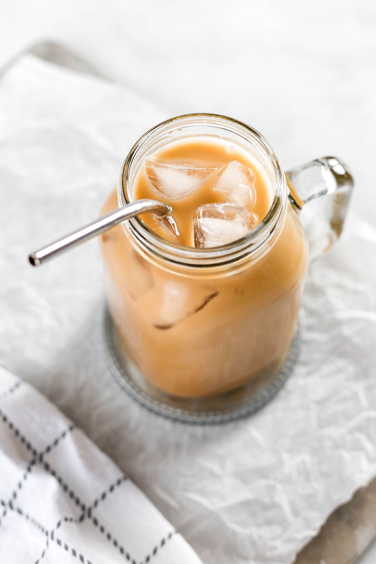 an almond milk iced latte in a large glass mug, sitting on a grey coaster