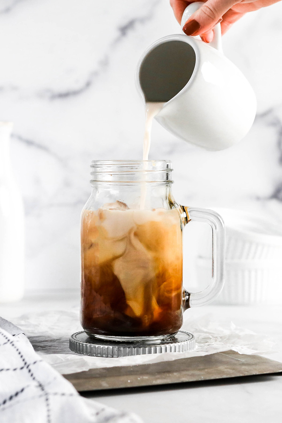 a hand pouring almond milk into an iced latte