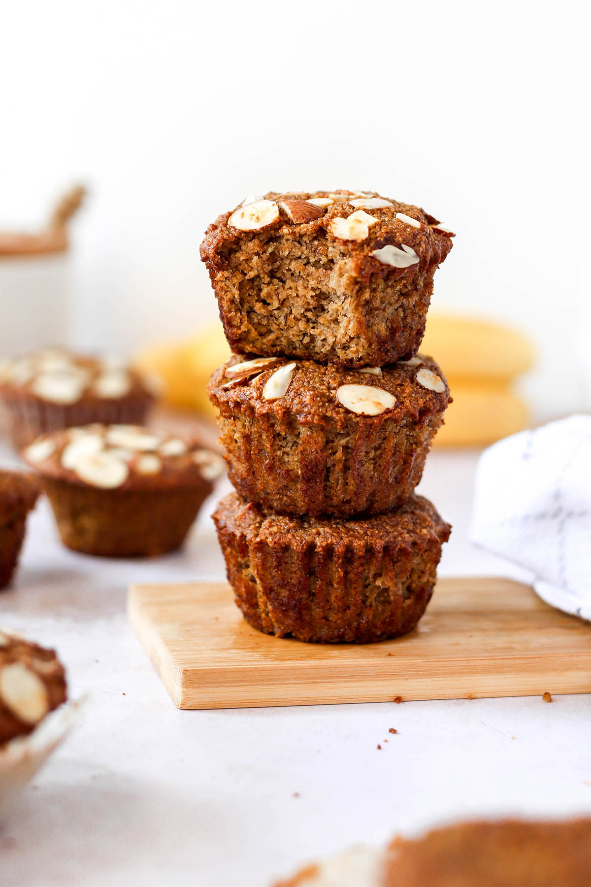 a stack of banana muffins with almond slices on top, and a bite missing from one of the muffins