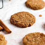 a vegan molasses cookie on a table with cinnamon sticks