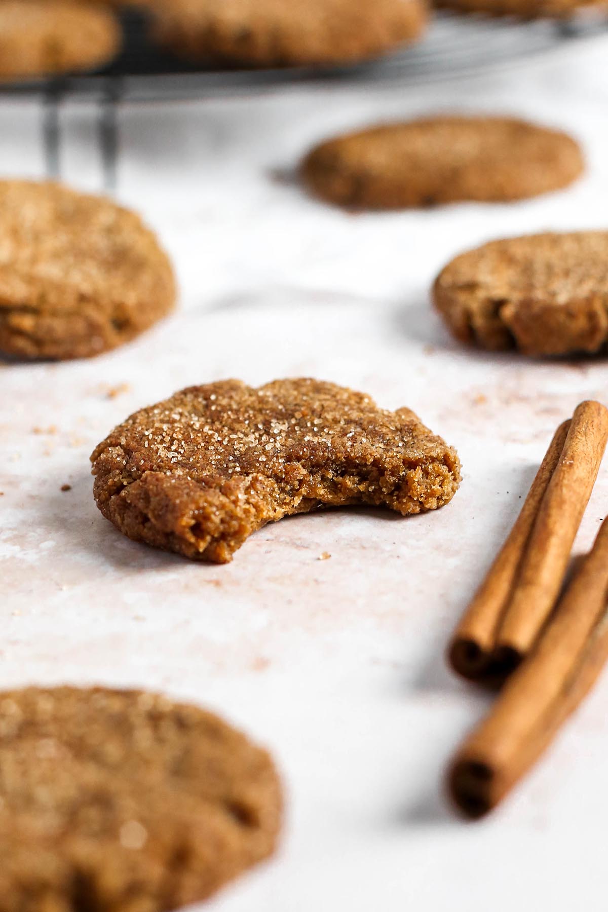 a ginger molasses cookie on a table, with a bite missing from the cookie. There are cinnamon sticks around.