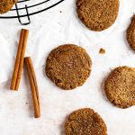 multiple vegan cookies on a table with cinnamon sticks around