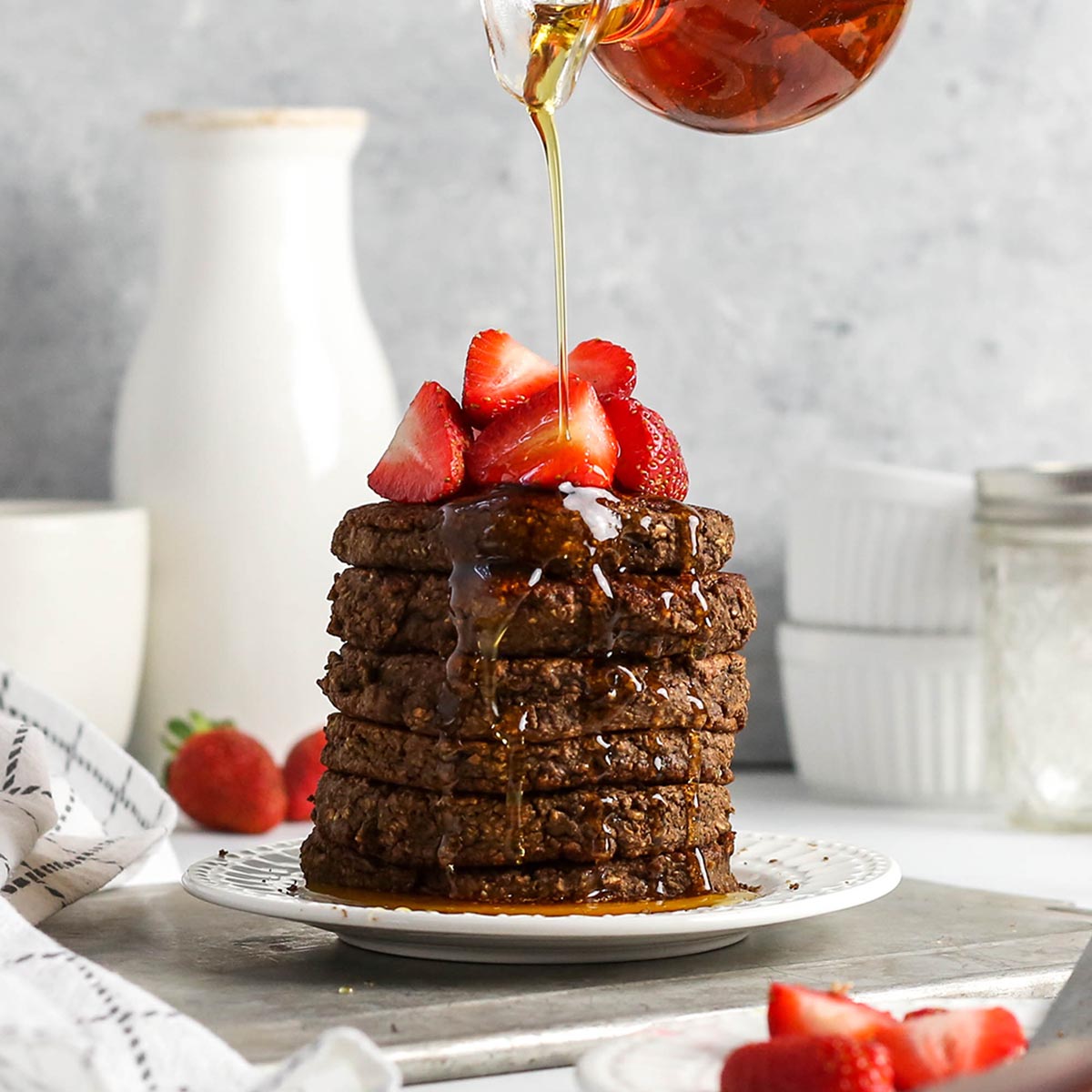 a stack of chocolate pancakes with maple syrup flowing down the side