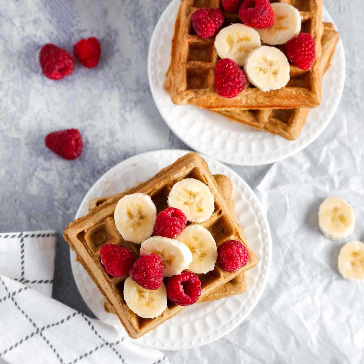 two plates of dairy free waffles with bananas and raspberries on top