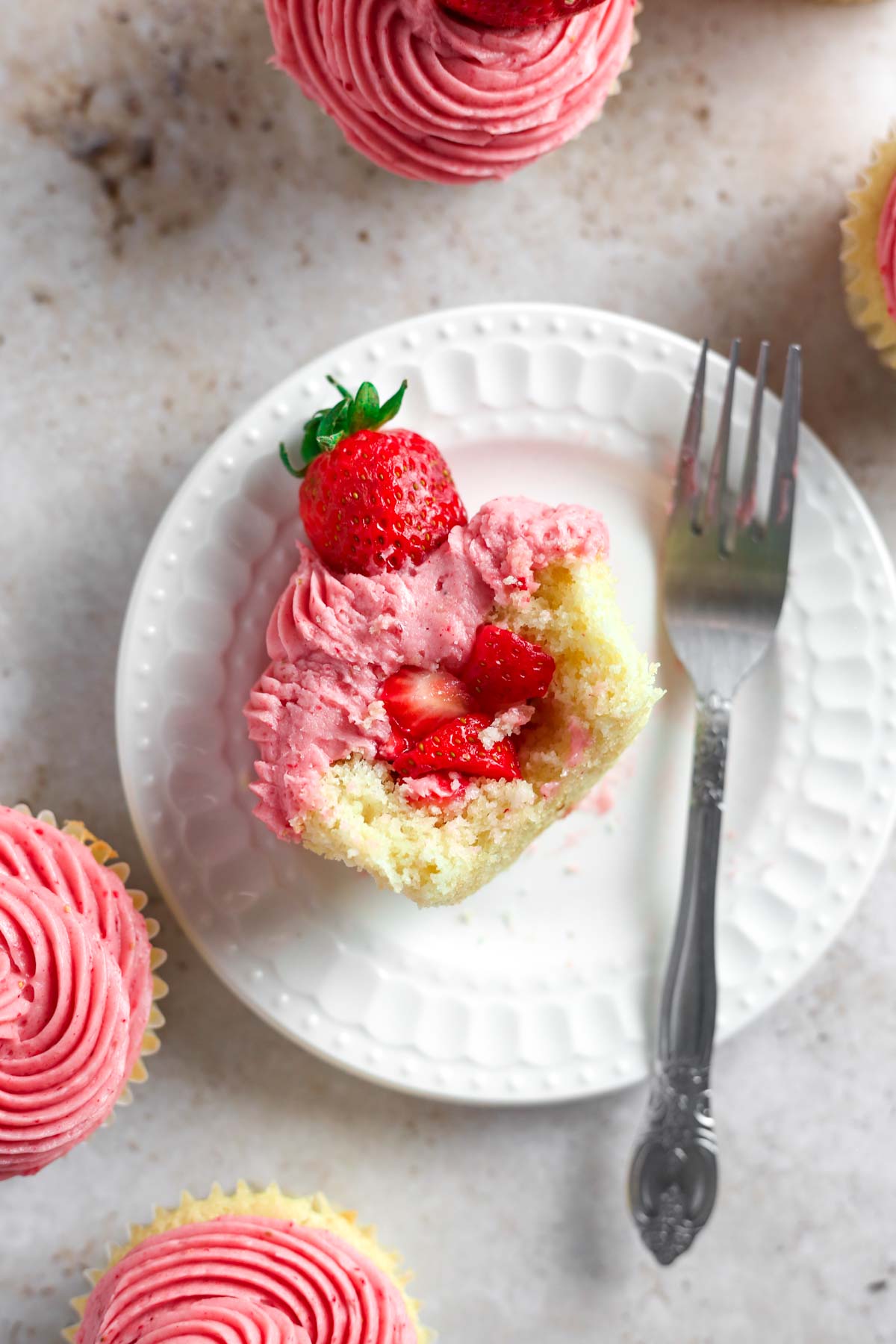 a strawberry cupcake on a small white plate with strawberry filling inside and a fork on the plate.