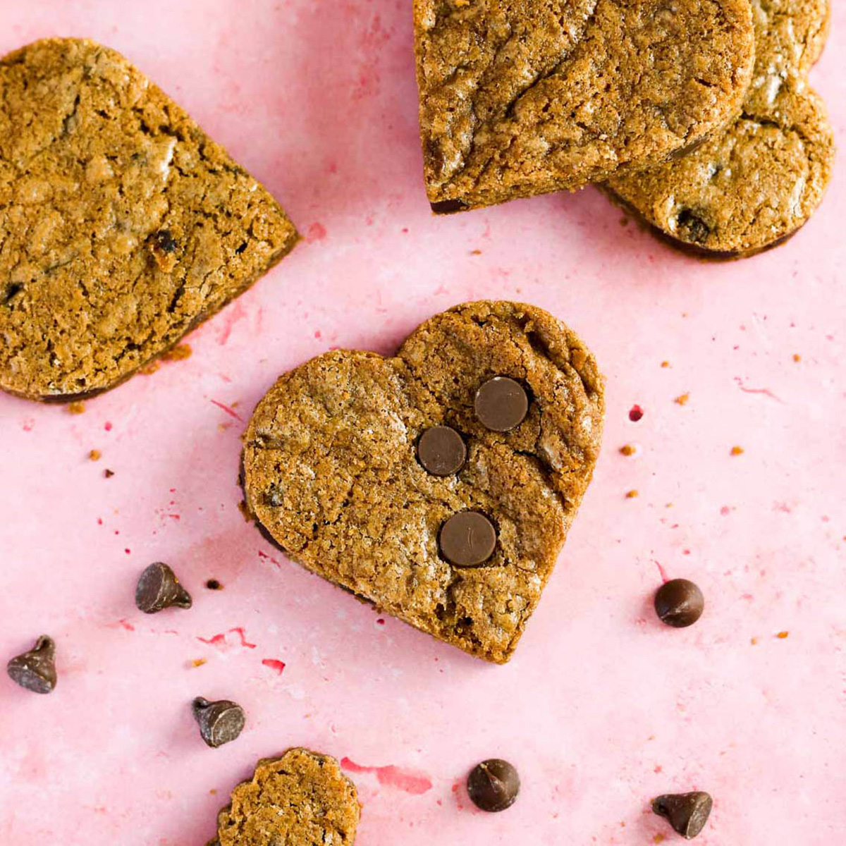 a few heart shaped chocolate chip cookies on a pink surface