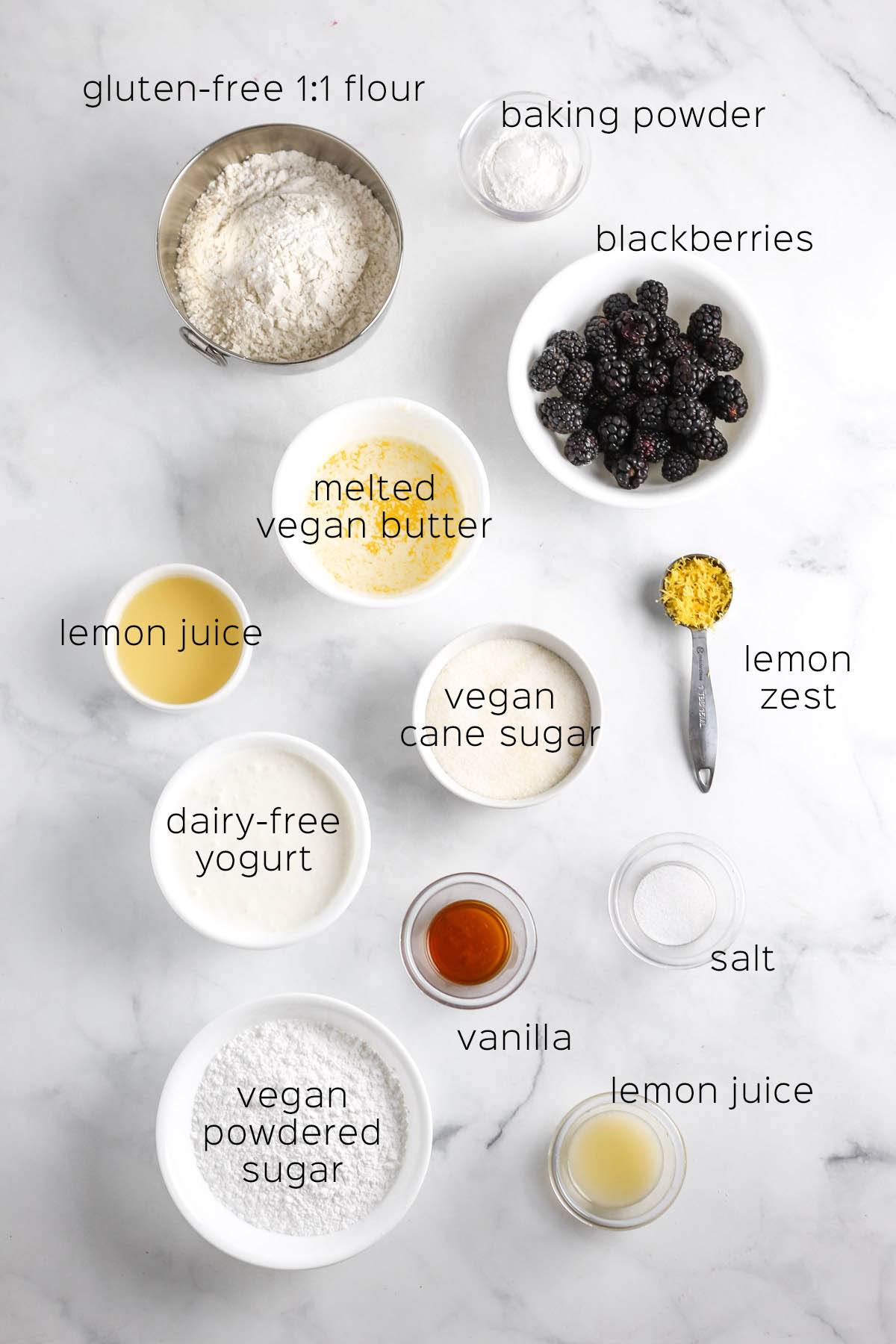 the ingredients to make the lemon bread, shown in individual bowls on a marble table.