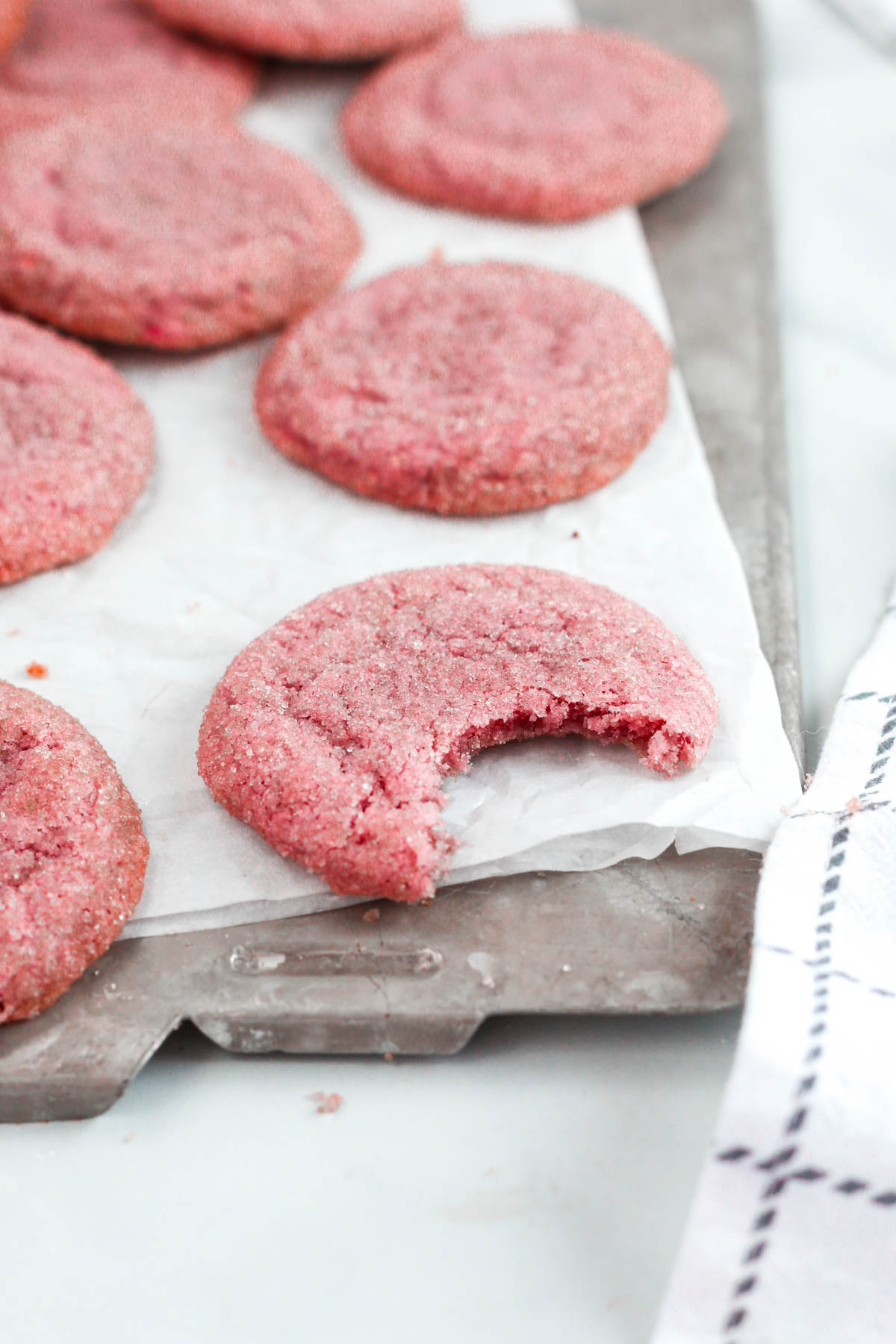 a close up photo of a pink sugar cookie on a baking tray, with a bite missing from the cookie.