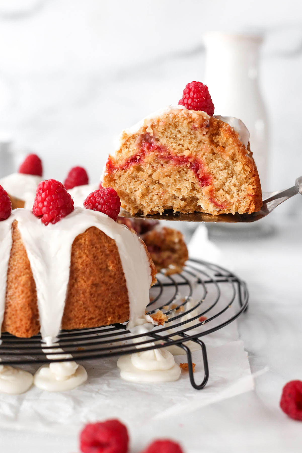 a slice of cake being lifted from the tray with the white chocolate raspberry bundt cake, showing the raspberry jam inside.
