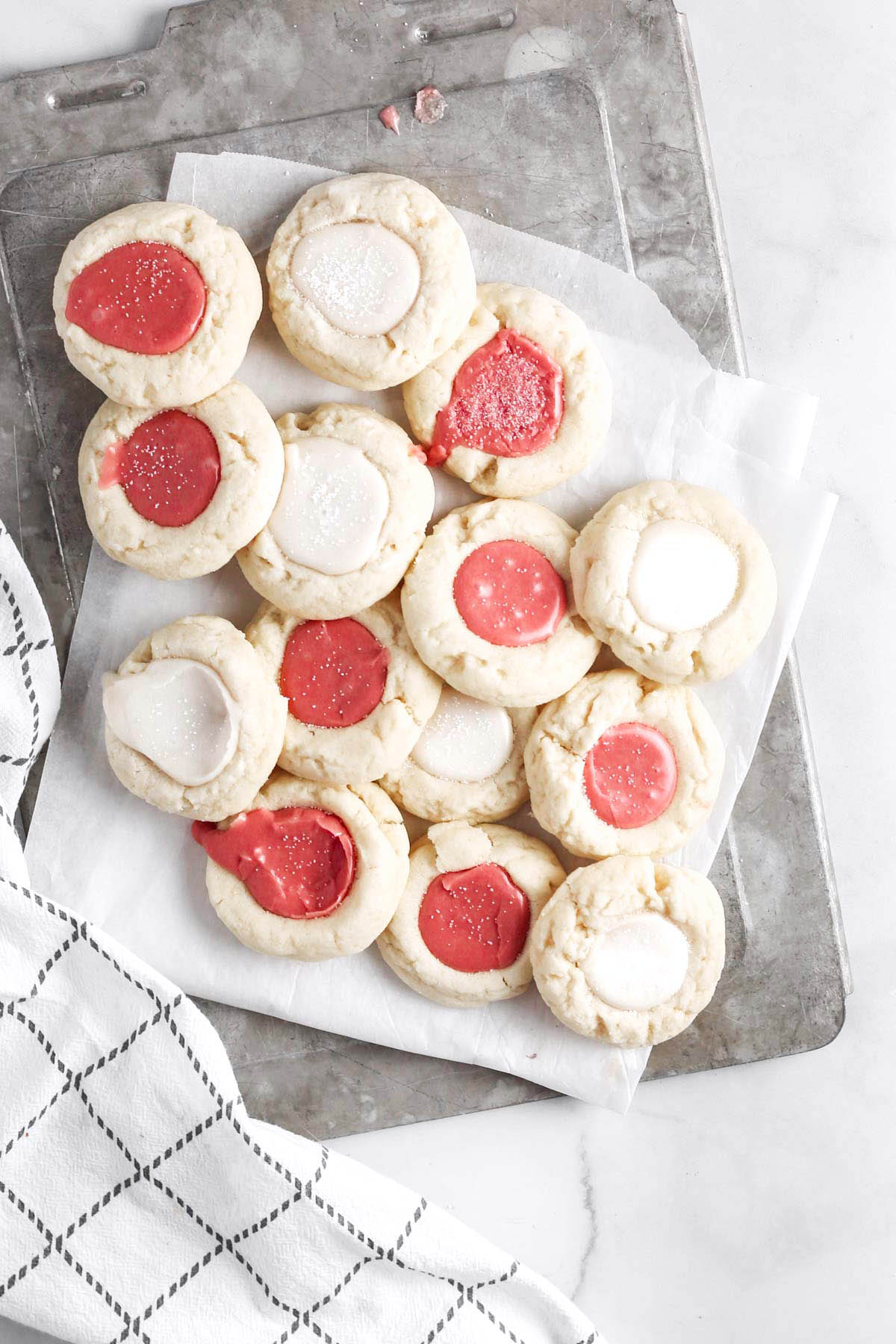 a dozen thumbprint cookies with icing on a grey tray for serving.