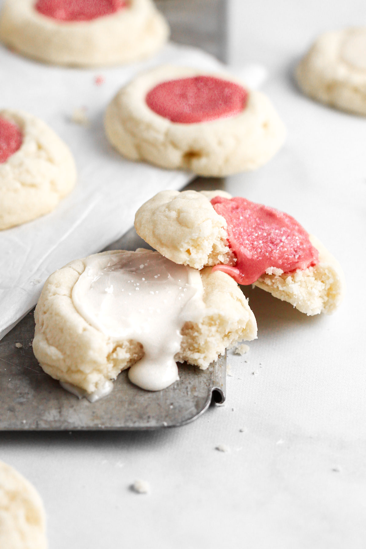 two thumbprint cookies leaning against each other, with the icing in the center spilling out and running down the side of the cookies.